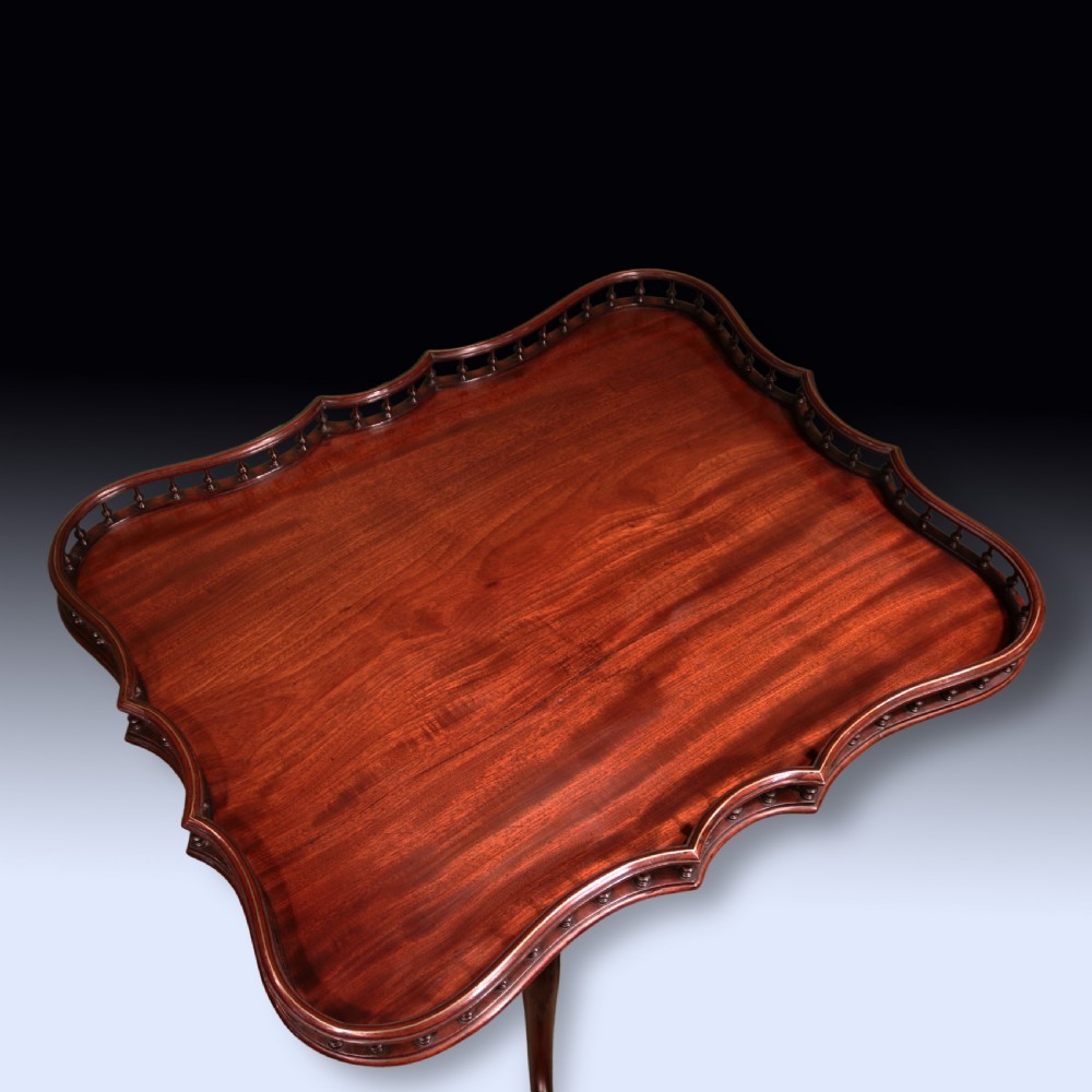 A George III mahogany tripod table featuring a rectangular serpentine top with a pierced spindle gallery on a carved pillar and cabriole legs. View II