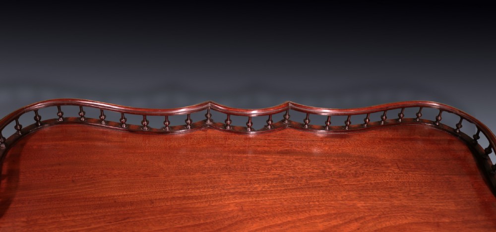 A George III mahogany tripod table featuring a rectangular serpentine top with a pierced spindle gallery on a carved pillar and cabriole legs. View IV