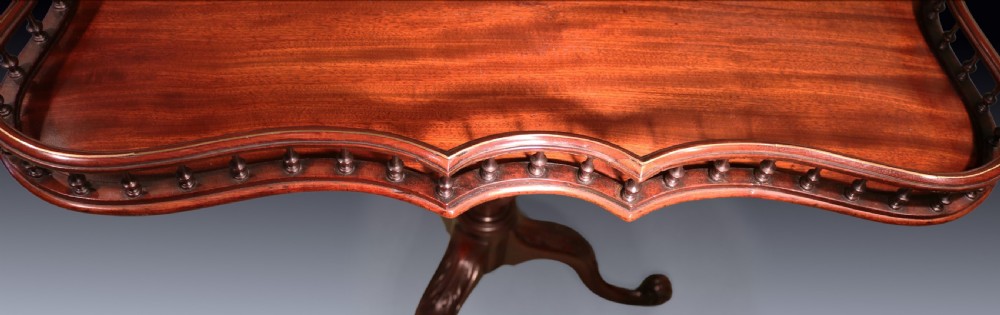A George III mahogany tripod table featuring a rectangular serpentine top with a pierced spindle gallery on a carved pillar and cabriole legs. View V