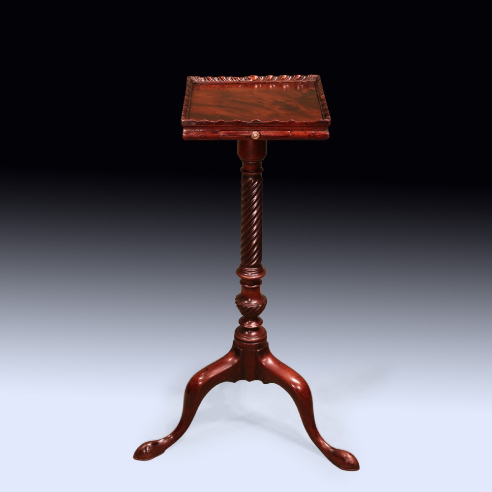 An antique George III mahogany kettle stand featuring a square tray top with a gallery rim, a pull-out slide, a spiral-carved column, and a tripod base.