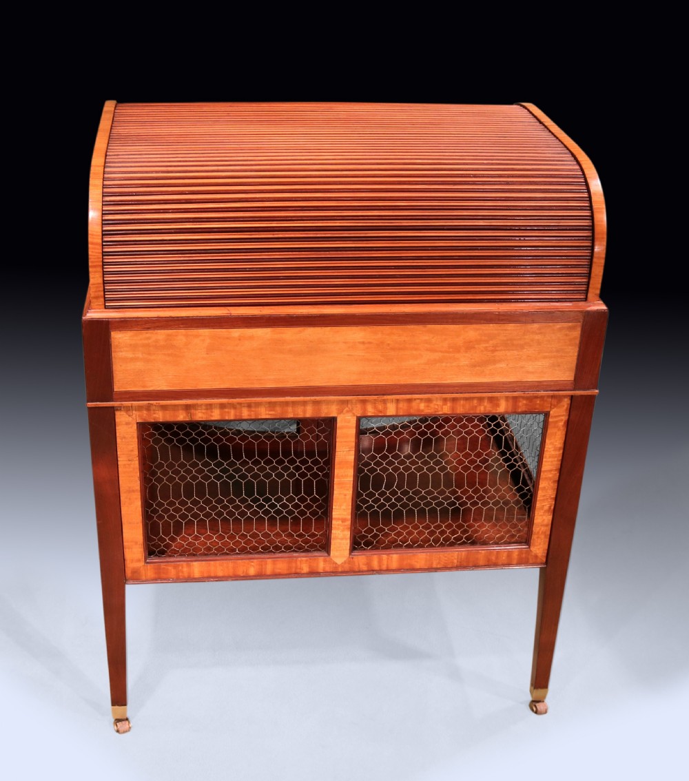 A George III mahogany and satinwood writing table featuring a roll-top compartment, green leather writing surface, inner drawers, and wire mesh lower panels on tapered legs with brass castors. View III
