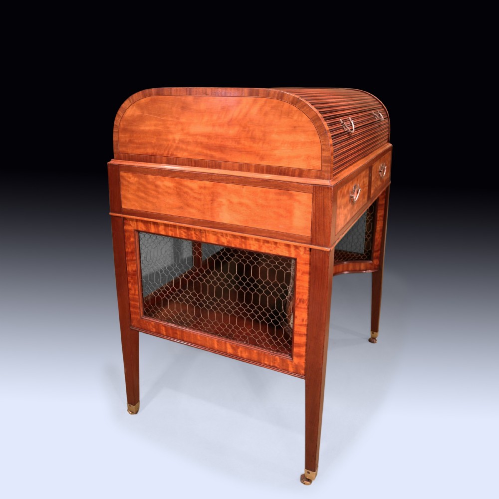 A George III mahogany and satinwood writing table featuring a roll-top compartment, green leather writing surface, inner drawers, and wire mesh lower panels on tapered legs with brass castors. View IV