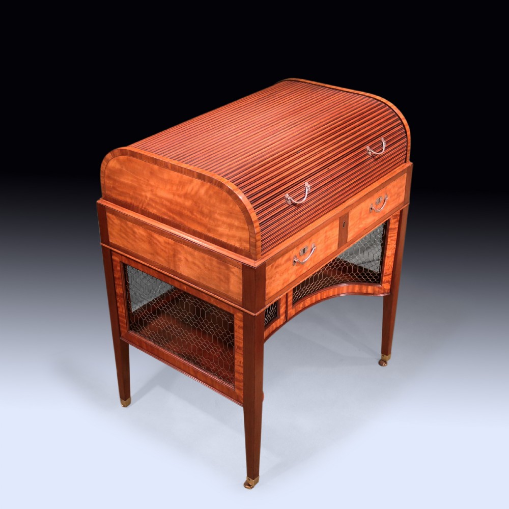 A George III mahogany and satinwood writing table featuring a roll-top compartment, green leather writing surface, inner drawers, and wire mesh lower panels on tapered legs with brass castors. View V