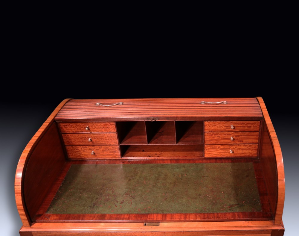 A George III mahogany and satinwood writing table featuring a roll-top compartment, green leather writing surface, inner drawers, and wire mesh lower panels on tapered legs with brass castors. View VI