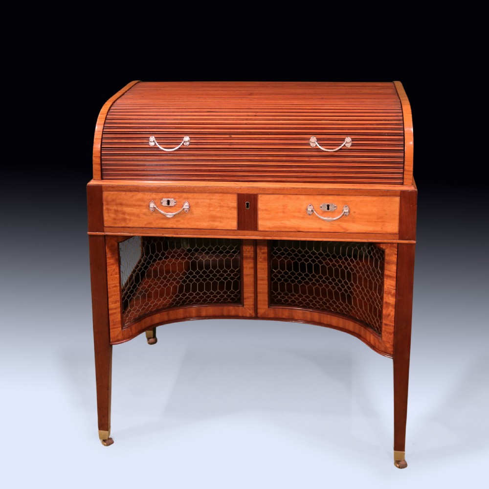 A George III mahogany and satinwood writing table featuring a roll-top compartment, green leather writing surface, inner drawers, and wire mesh lower panels on tapered legs with brass castors. View VII