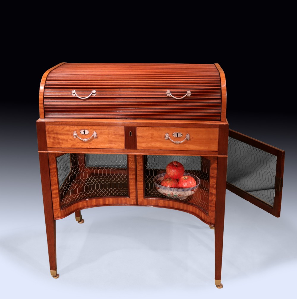 A George III mahogany and satinwood writing table featuring a roll-top compartment, green leather writing surface, inner drawers, and wire mesh lower panels on tapered legs with brass castors. View VIII