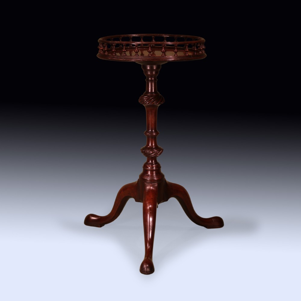 An 18th-century George III mahogany kettle stand featuring a circular top with a spindled gallery rim, supported by a turned column and tripod cabriole legs with pad feet.