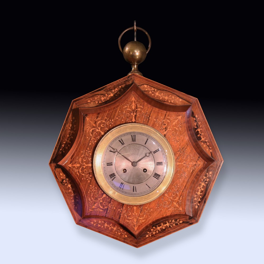 An octagonal nineteenth-century French rosewood wall clock decorated with floral marquetry inlay, a silvered dial with Roman numerals, and a top brass hanging ring.
