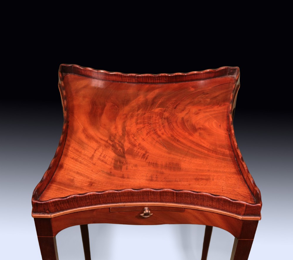 A late 18th-century Sheraton mahogany kettle stand featuring a scalloped gallery top, pull-out slide, and slender square tapered legs. View IV