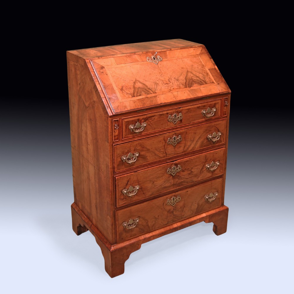 An eighteenth-century George II walnut bureau featuring a sloping fall-front lid over four graduated drawers with engraved brass handles and bracket feet.