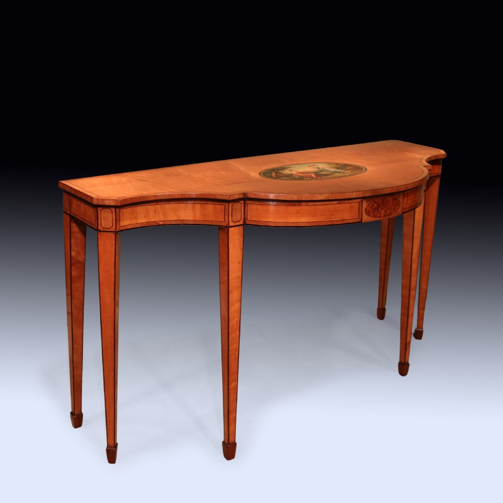 An antique Sheraton period satinwood console table featuring a curved front, hand-painted central medallion on top, crossbanded borders, and four square tapered legs. View IV