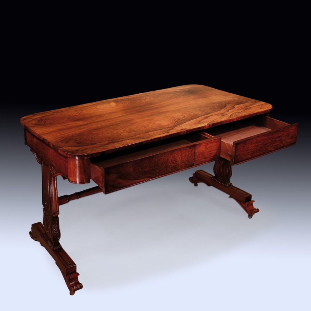 An early nineteenth-century Regency rosewood writing table featuring a rectangular top with rounded corners, frieze drawers, carved trestle supports, and a stretcher base.