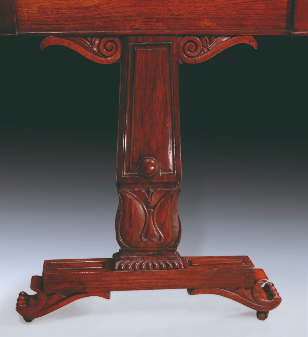 An early nineteenth-century Regency rosewood writing table featuring a rectangular top with rounded corners, frieze drawers, carved trestle supports, and a stretcher base. View II