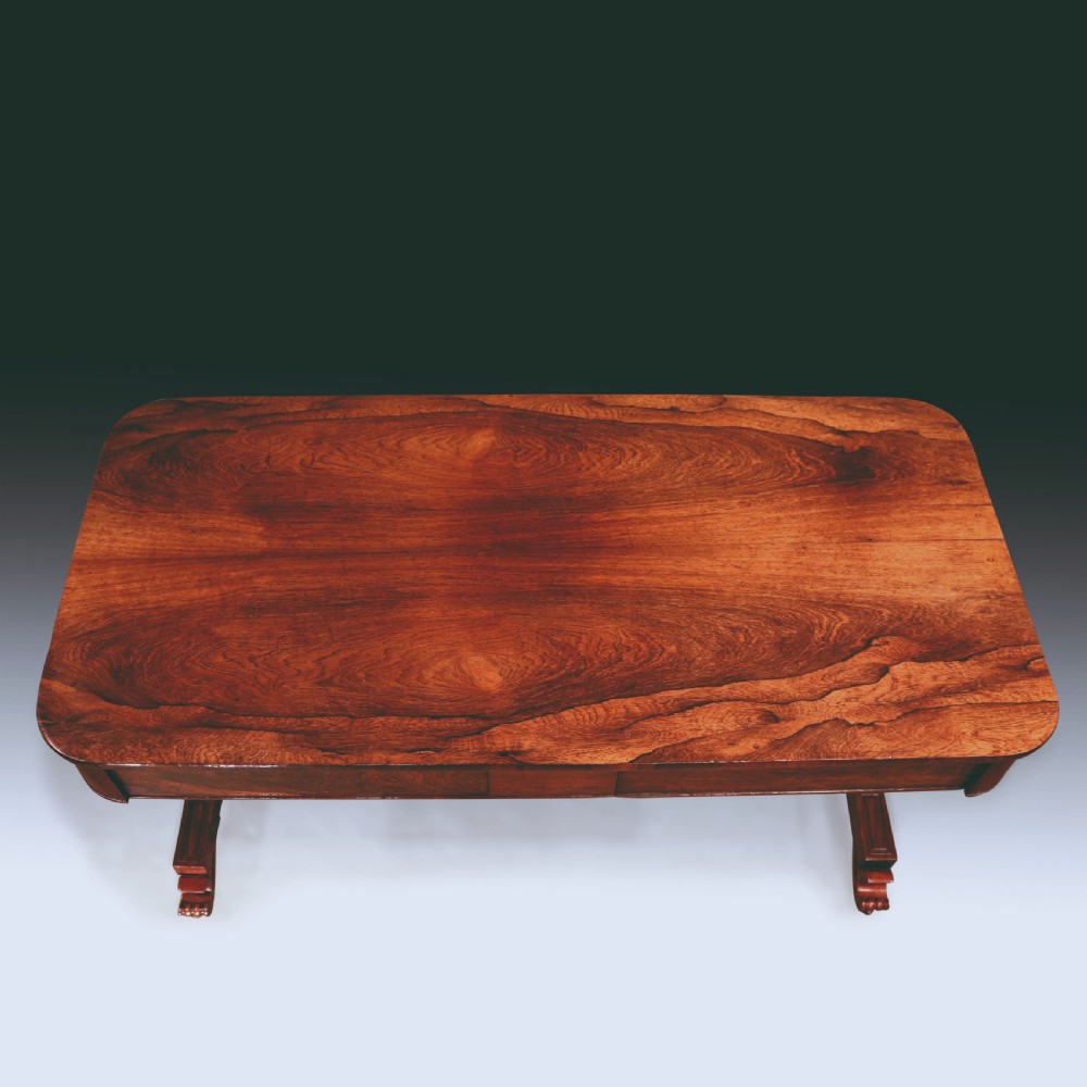 An early nineteenth-century Regency rosewood writing table featuring a rectangular top with rounded corners, frieze drawers, carved trestle supports, and a stretcher base. View III