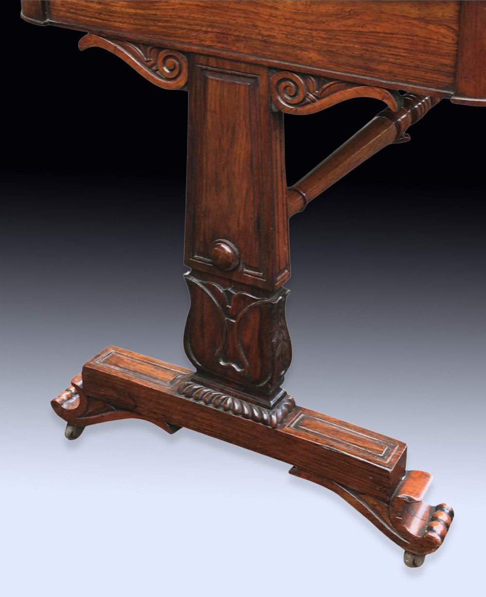 An early nineteenth-century Regency rosewood writing table featuring a rectangular top with rounded corners, frieze drawers, carved trestle supports, and a stretcher base. View IV