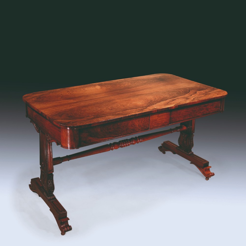 An early nineteenth-century Regency rosewood writing table featuring a rectangular top with rounded corners, frieze drawers, carved trestle supports, and a stretcher base. View V