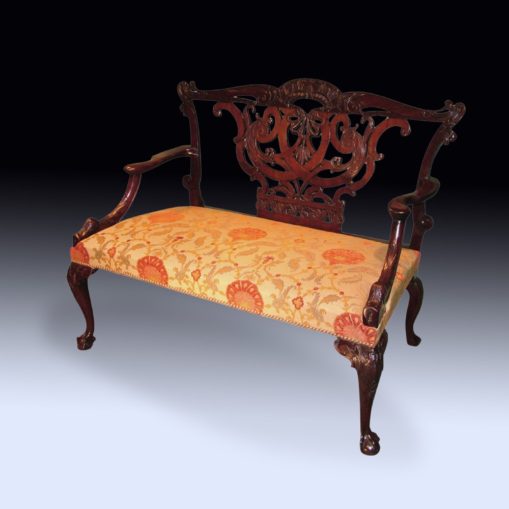 An 18th-century Chippendale mahogany two-seat settee featuring an intricately carved pierced back splat, curved armrests, cabriole legs, and a patterned yellow fabric upholstered seat.