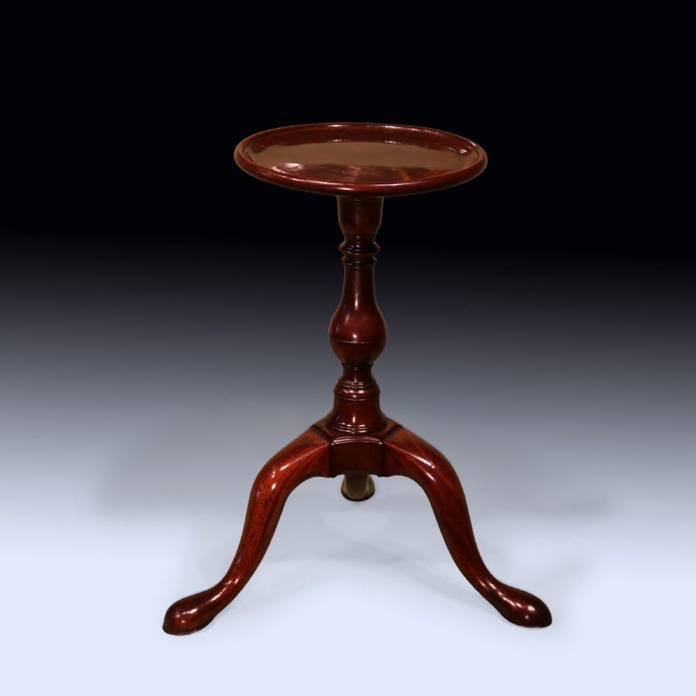An 18th-century George II mahogany kettle stand with a circular dished top, a central turned baluster stem, and three cabriole legs.