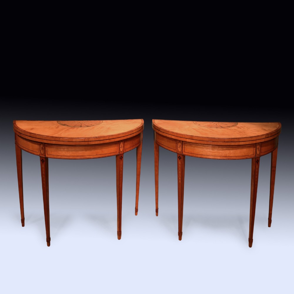 A pair of demilune antique satinwood card tables featuring central fan marquetry inlays and slender tapered legs.