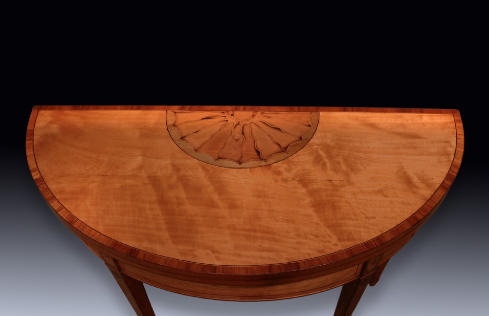 A pair of demilune antique satinwood card tables featuring central fan marquetry inlays and slender tapered legs. View VI