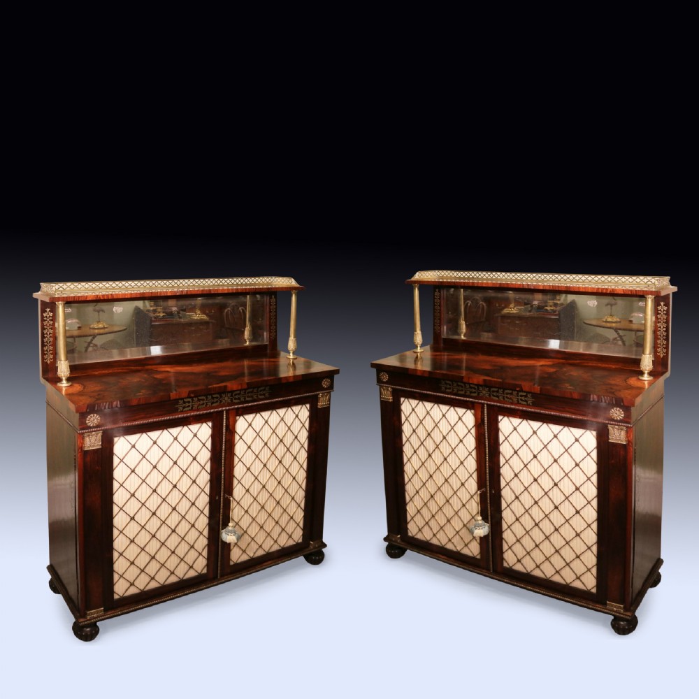 A matching pair of dark rosewood Regency side cabinets featuring brass inlay, mirrored top tiers with brass galleries, and pleated fabric behind brass grilles on the doors.