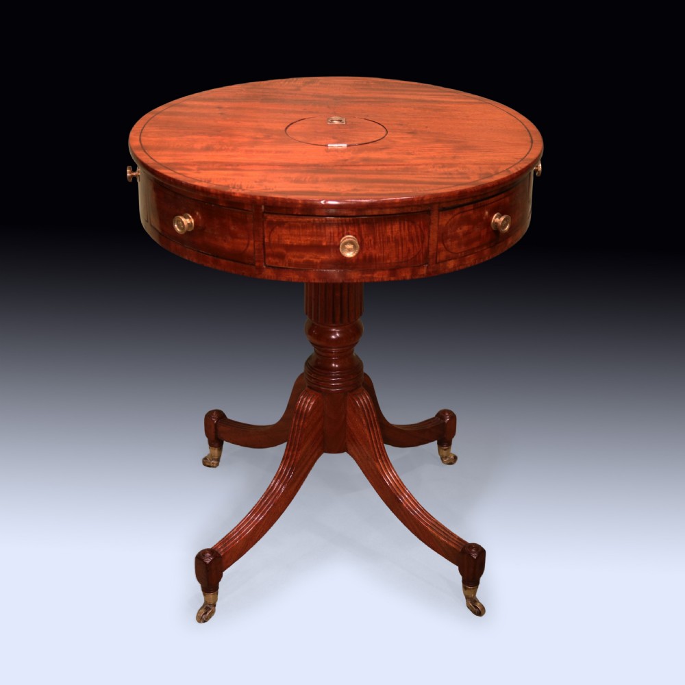 An early 19th-century circular mahogany drum table with perimeter drawers, a reeded central pedestal, and four splayed legs with brass castors.