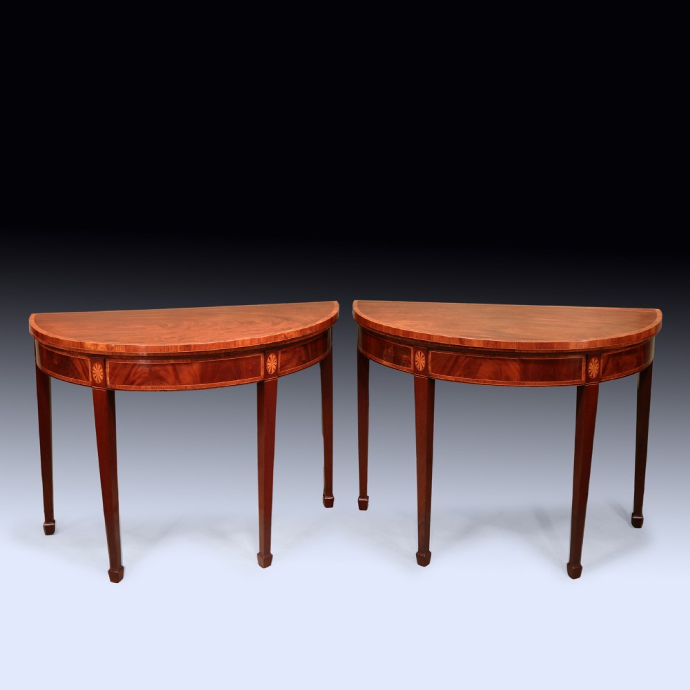 A pair of late 18th-century semi-circular mahogany card tables featuring inlaid rosettes and square tapered legs.