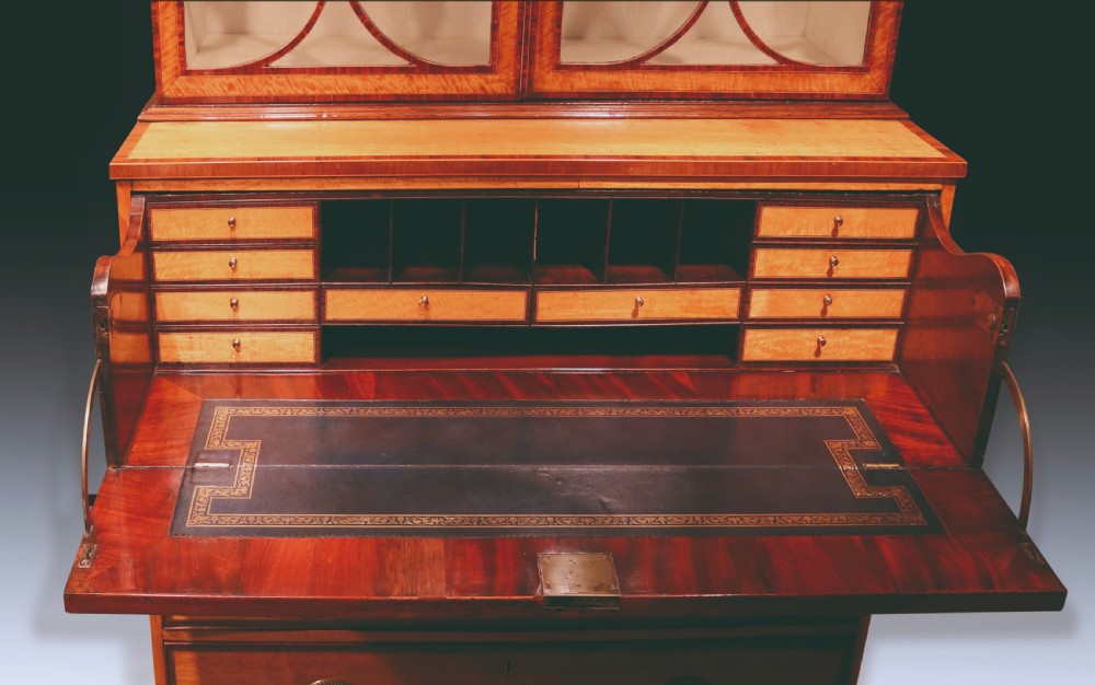 A Sheraton period satinwood secretaire bookcase featuring astagal glazed doors on the upper display cabinet over a chest of drawers. View VII