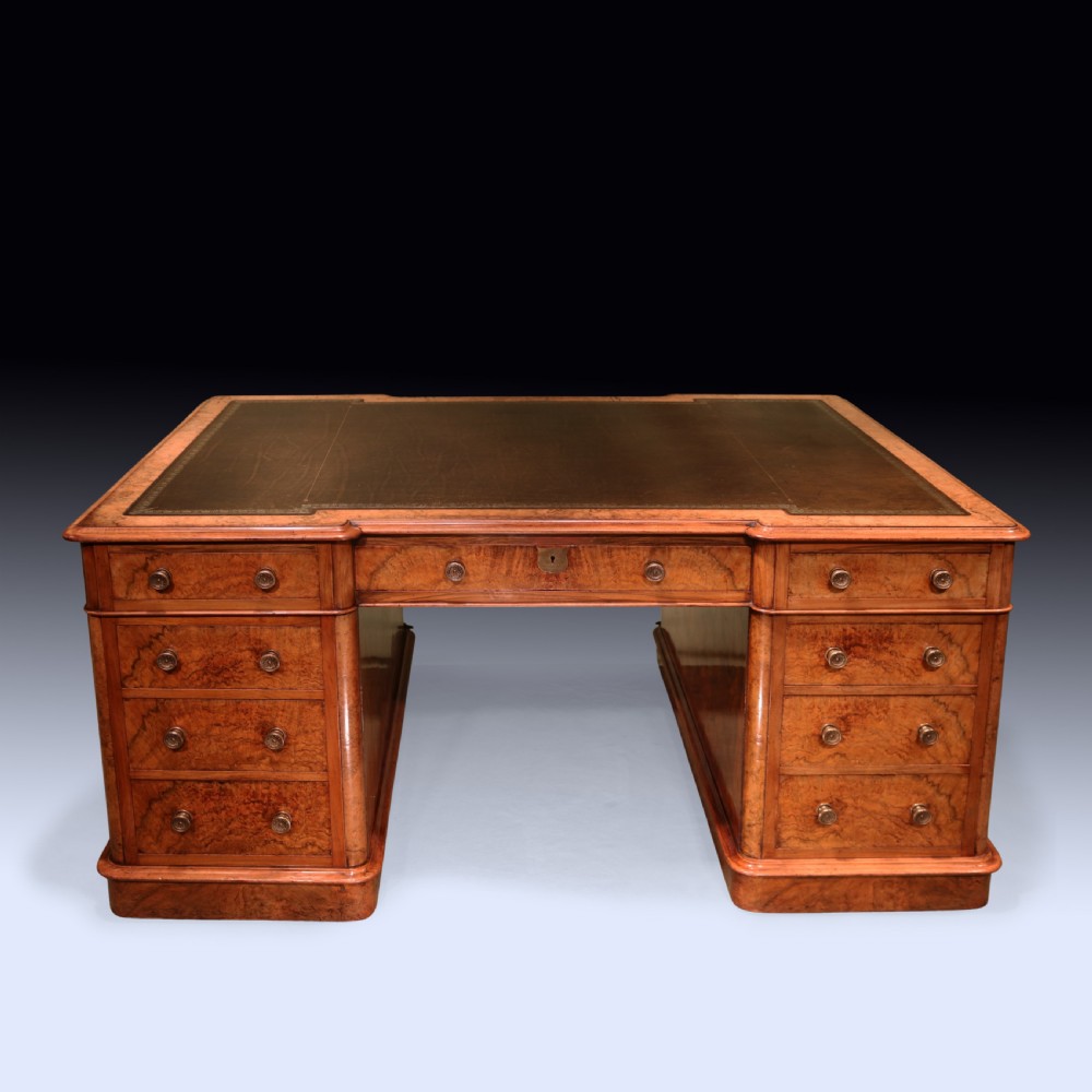 A mid 19th-century Victorian burr walnut pedestal desk featuring a green leather inset top, rounded corners, multiple drawers with turned wooden knobs, and a plinth base. View II
