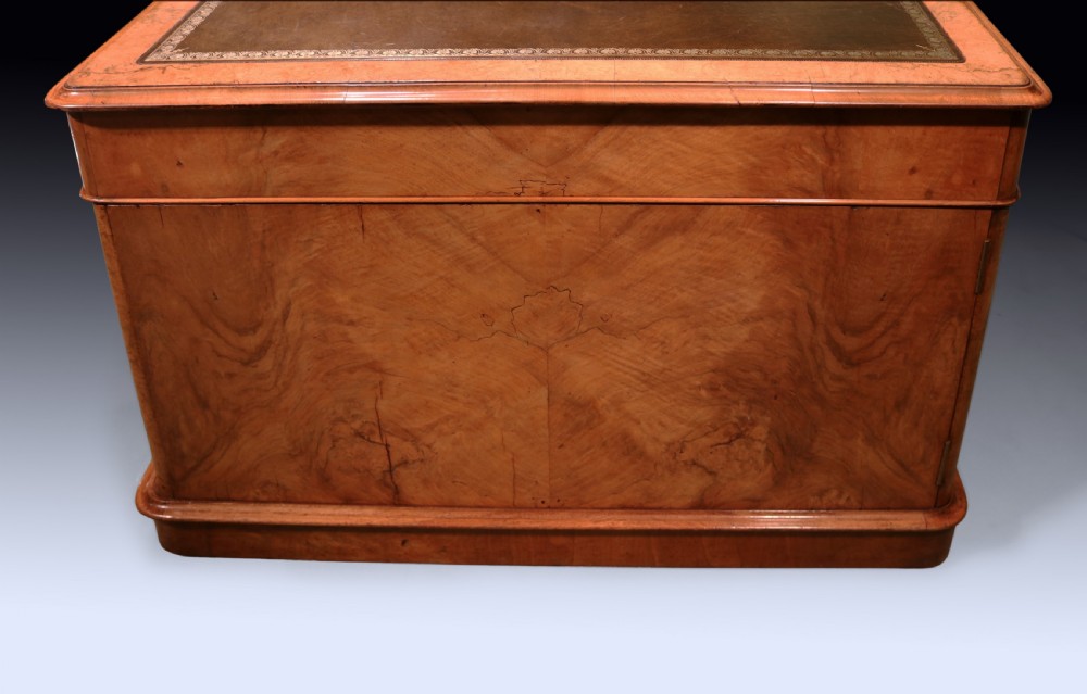 A mid 19th-century Victorian burr walnut pedestal desk featuring a green leather inset top, rounded corners, multiple drawers with turned wooden knobs, and a plinth base. View III