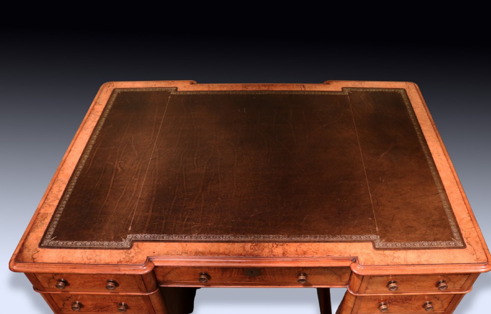 A mid 19th-century Victorian burr walnut pedestal desk featuring a green leather inset top, rounded corners, multiple drawers with turned wooden knobs, and a plinth base. View IV
