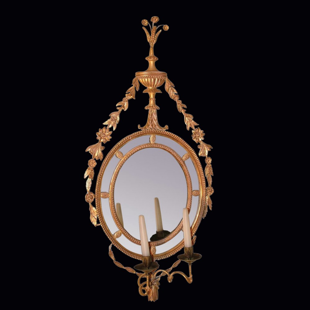 A pair of late 18th-century Neoclassical oval giltwood girandole mirrors with floral swags, urn finials, and twin candle branches. View II