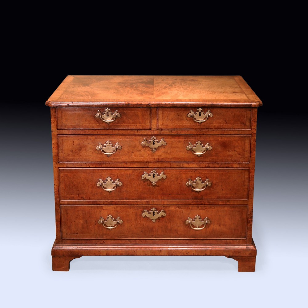 A George II period walnut chest of drawers featuring two short drawers over three long graduated drawers with brass handles and bracket feet.