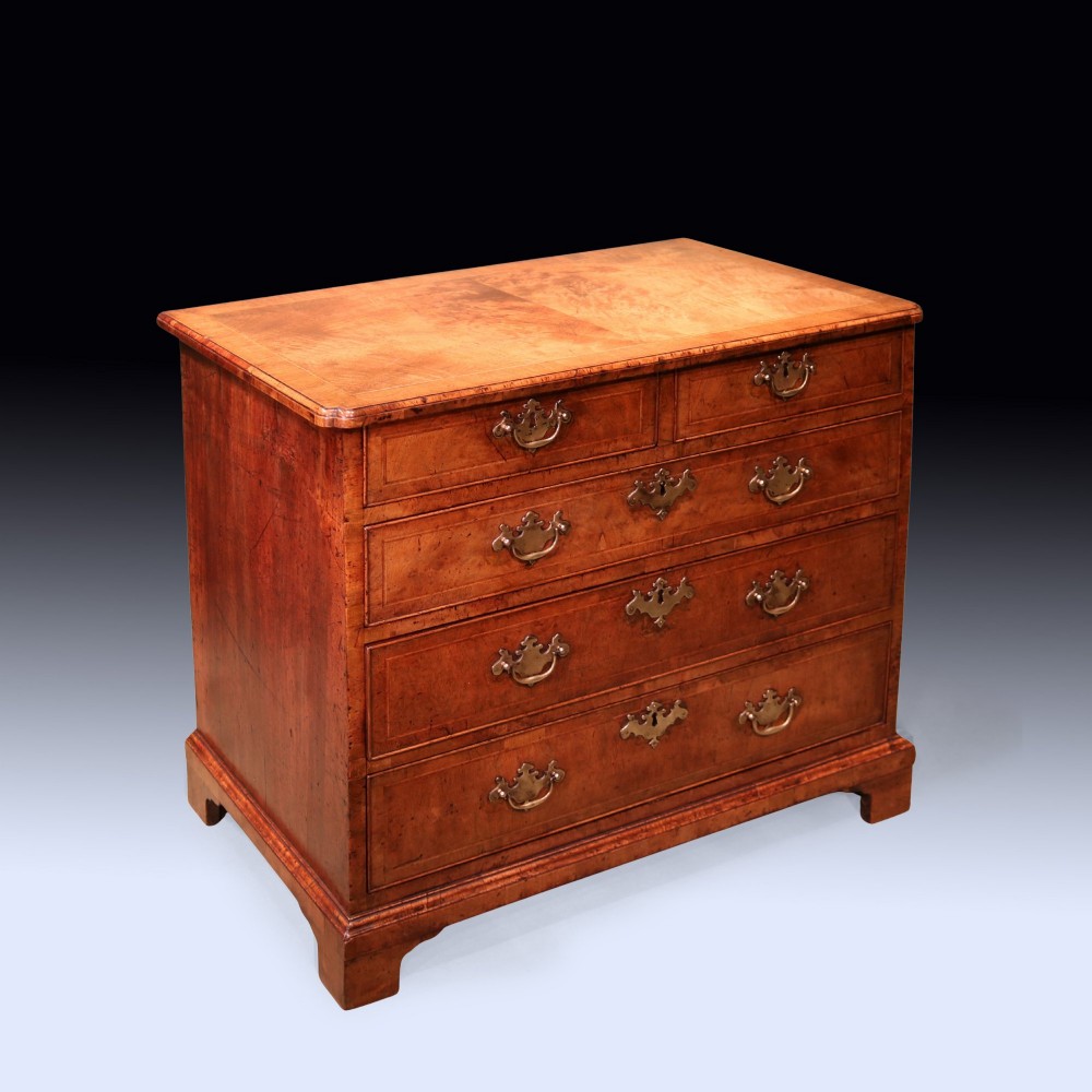 A George II period walnut chest of drawers featuring two short drawers over three long graduated drawers with brass handles and bracket feet. View II