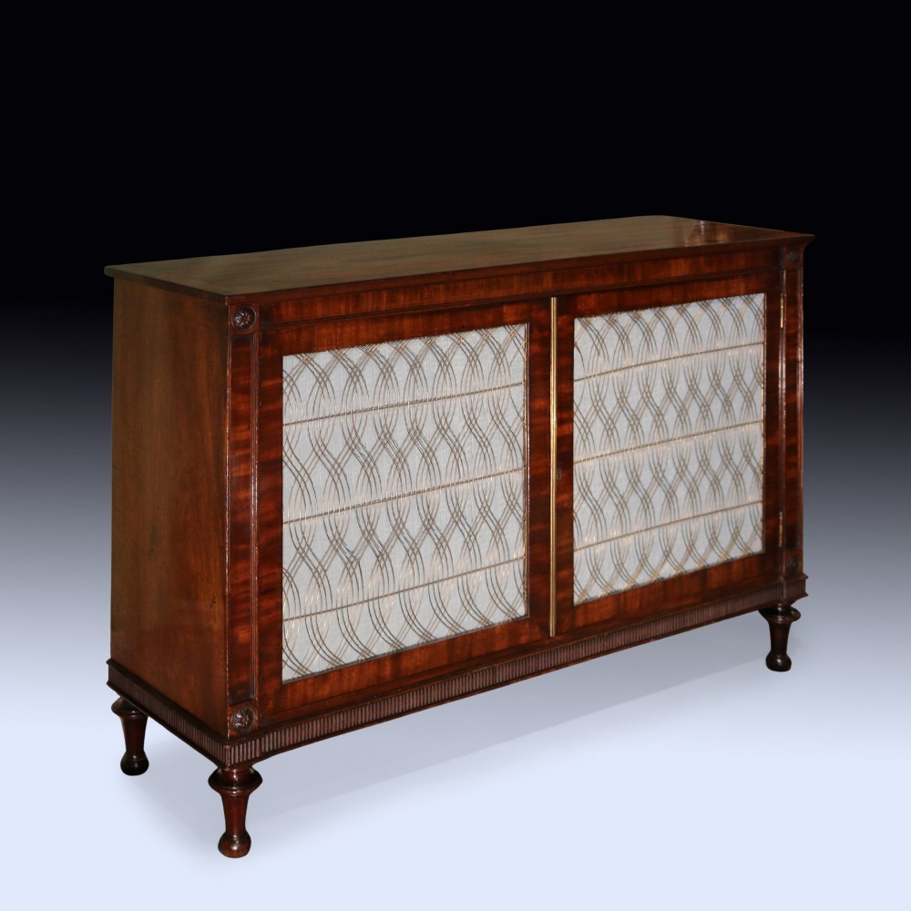 A Regency period two-door mahogany side cabinet featuring brass wire grille panels lined with pleated fabric and raised on turned legs.