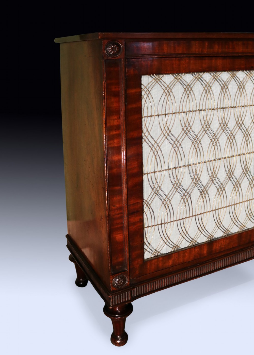 A Regency period two-door mahogany side cabinet featuring brass wire grille panels lined with pleated fabric and raised on turned legs. View II