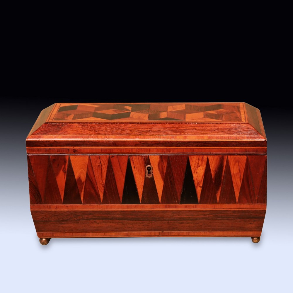 A Regency period wooden tea caddy featuring geometric parquetry inlay, a hinged lid, and small brass feet.