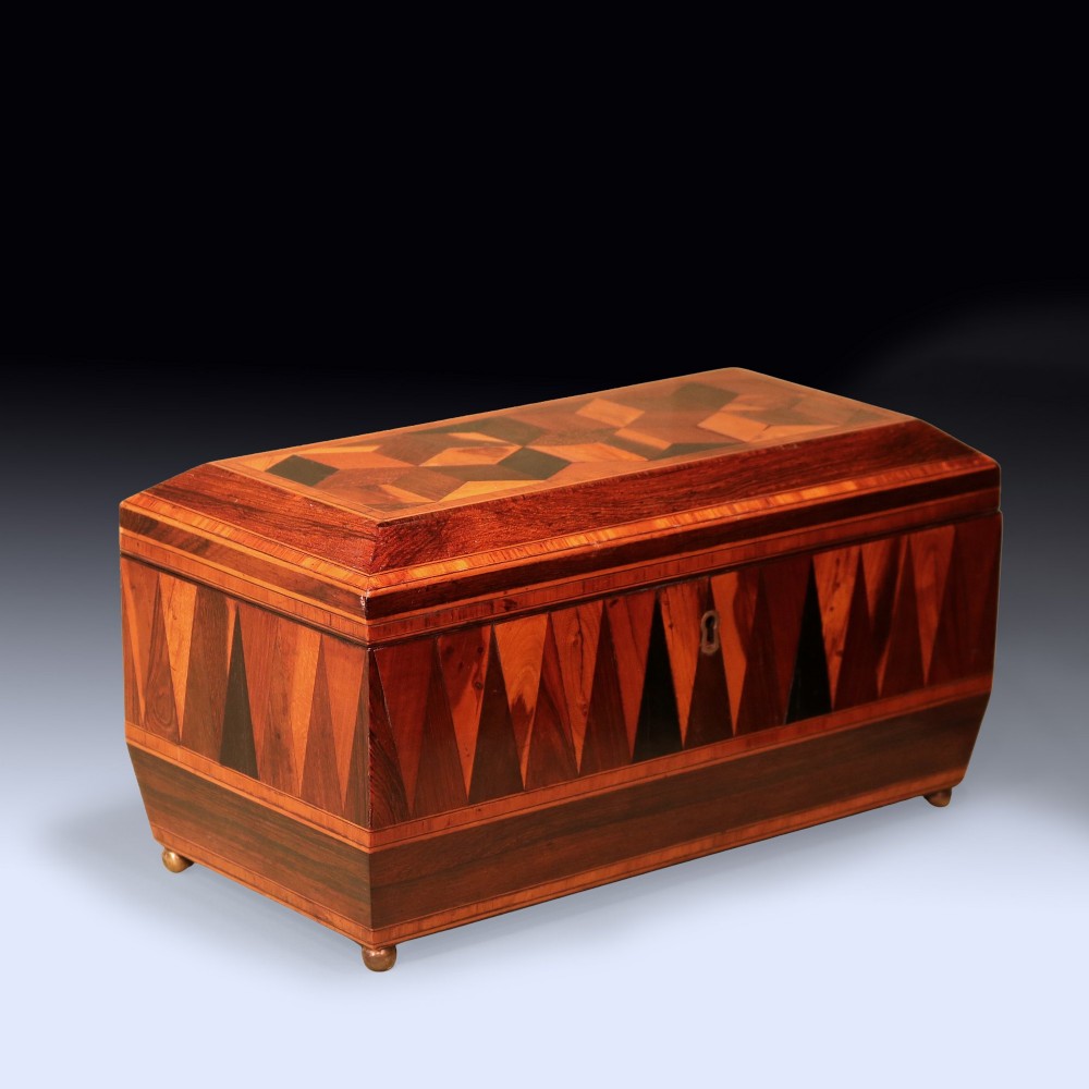 A Regency period wooden tea caddy featuring geometric parquetry inlay, a hinged lid, and small brass feet. View II