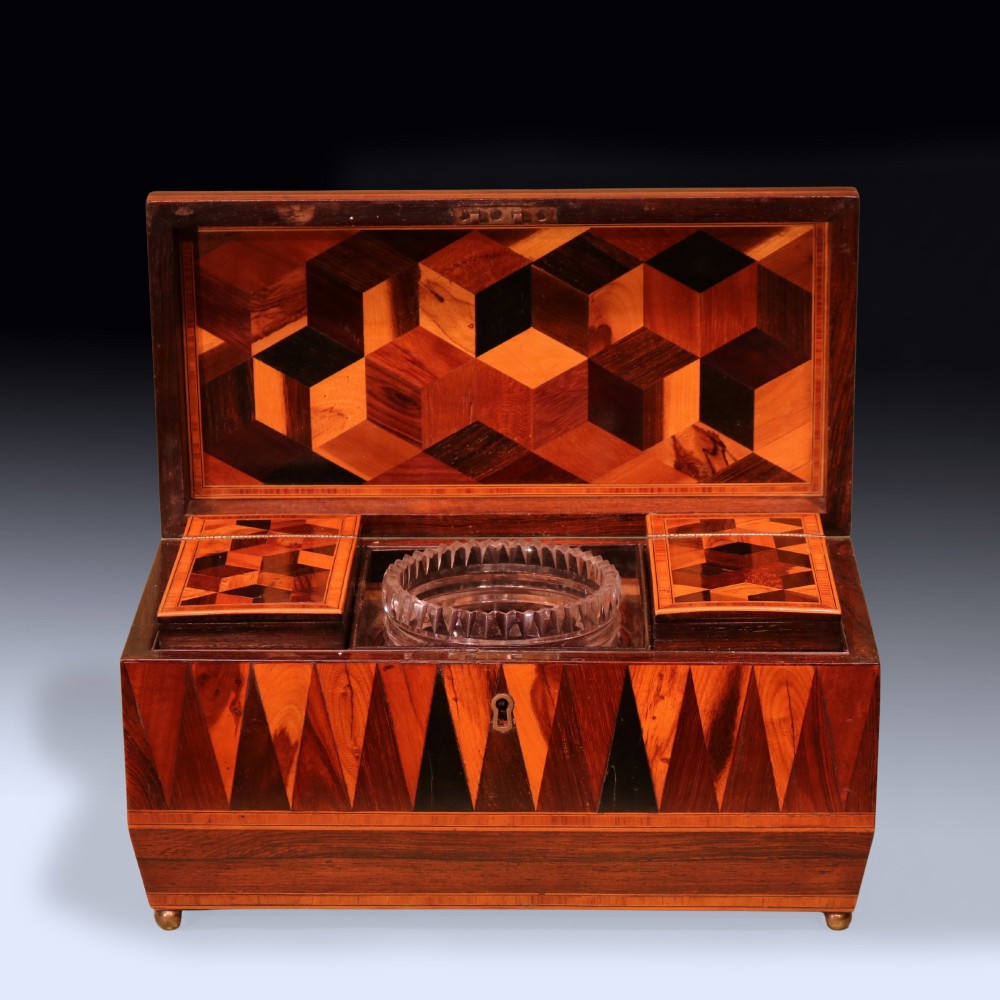 A Regency period wooden tea caddy featuring geometric parquetry inlay, a hinged lid, and small brass feet. View IV