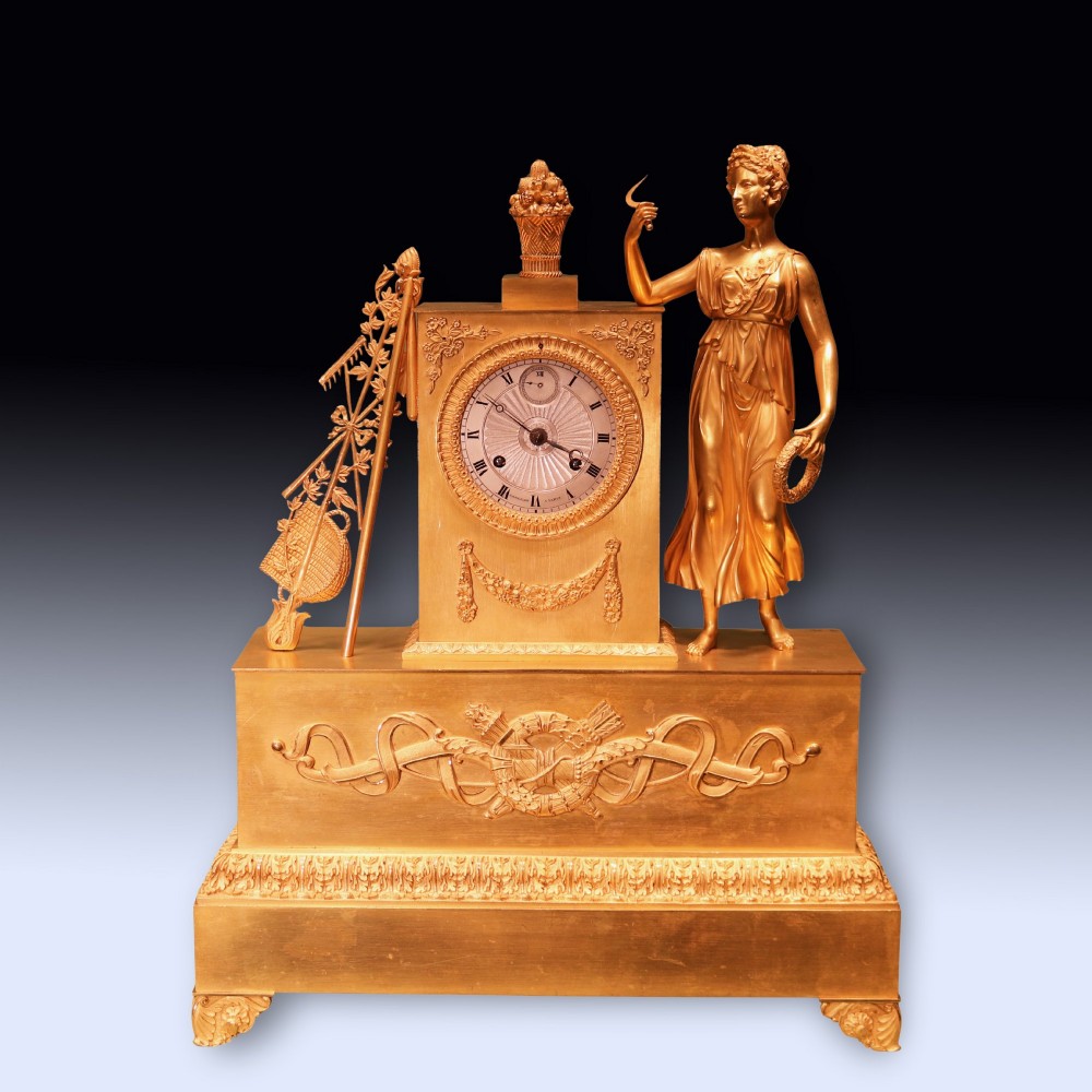 An early 19th-century French gilt bronze ormolu clock featuring a classical female figure standing beside a rectangular housing topped with a fruit basket.