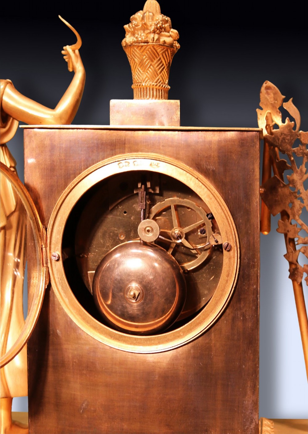 An early 19th-century French gilt bronze ormolu clock featuring a classical female figure standing beside a rectangular housing topped with a fruit basket. View VI