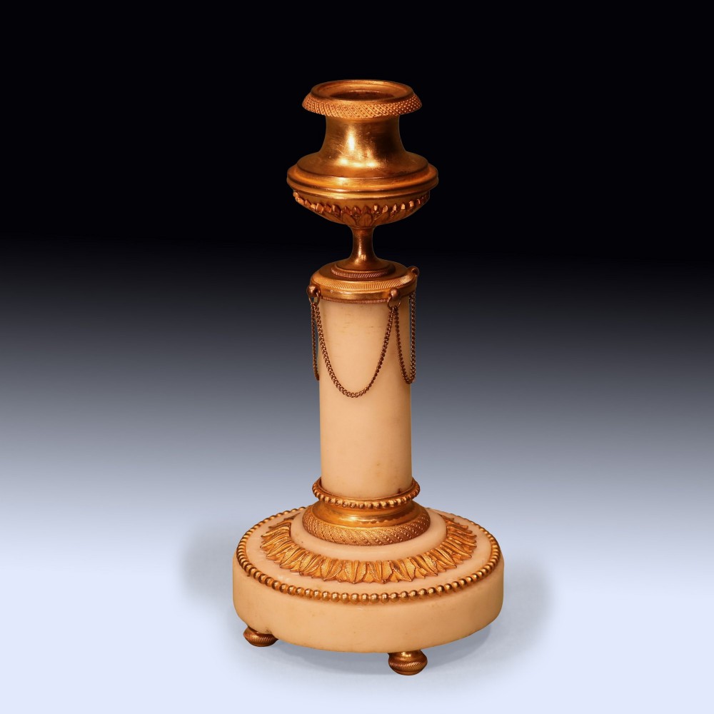 A pair of 19th-century Neoclassical candlesticks featuring white marble cylindrical columns adorned with gilt bronze chain swags and urn-shaped sconces resting on circular bases. View II