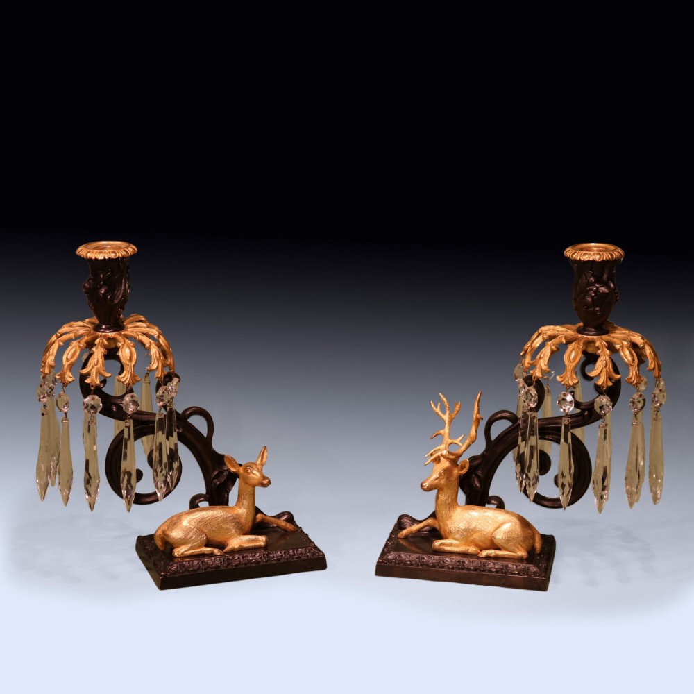 A pair of 19th-century dark bronze candlesticks featuring gilt ormolu figures of a stag and a doe sitting beneath glass prism lustres.