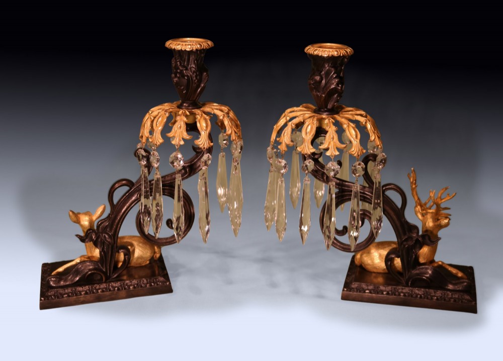 A pair of 19th-century dark bronze candlesticks featuring gilt ormolu figures of a stag and a doe sitting beneath glass prism lustres. View II