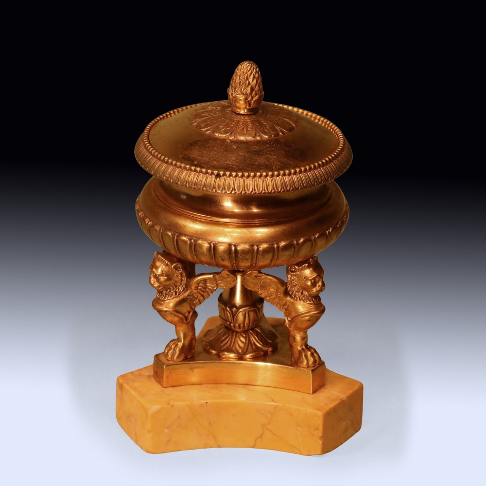 An early 19th-century urn-shaped ormolu inkwell supported by three winged lion monopodia legs on a shaped yellow Sienna marble base.
