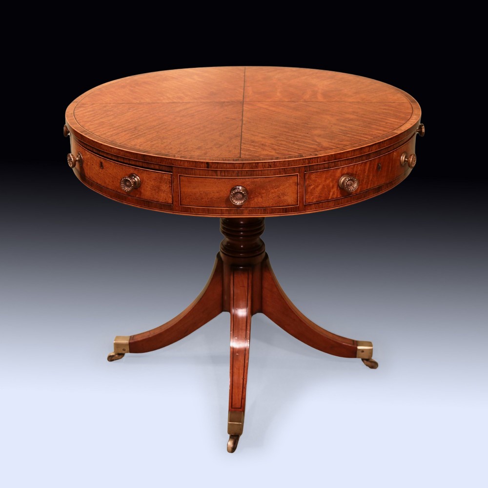 A George III mahogany drum table featuring a circular top with drawers around the apron, supported by a turned pedestal column and four splayed legs with brass castors.