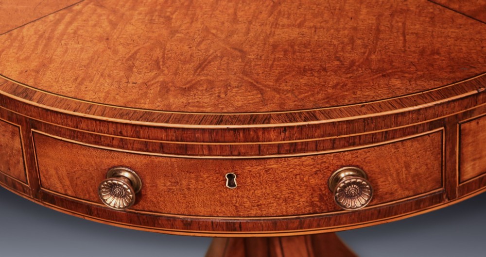 A George III mahogany drum table featuring a circular top with drawers around the apron, supported by a turned pedestal column and four splayed legs with brass castors. View III