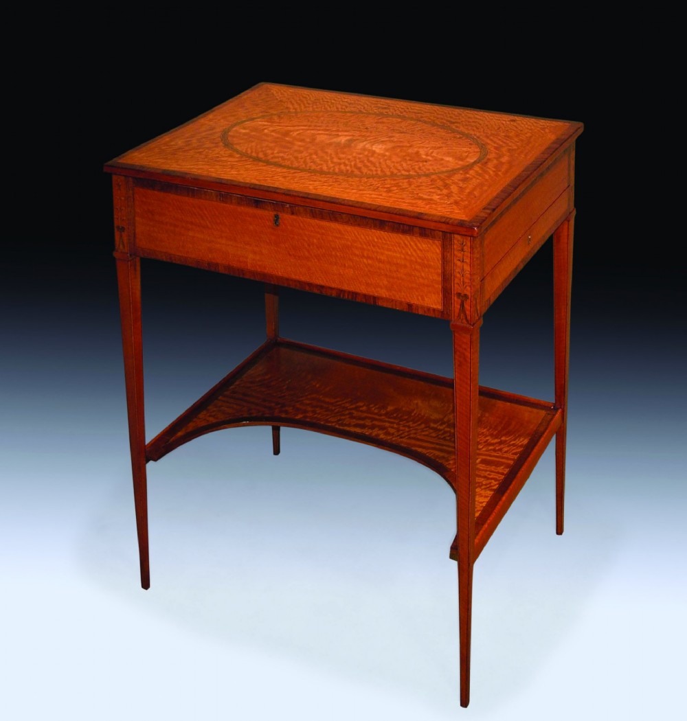 An antique Sheraton period satinwood occasional table featuring a rectangular top with an oval central inlay, a single drawer, tapered square legs, and a concave undertier.