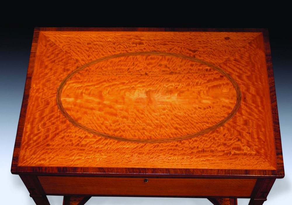 An antique Sheraton period satinwood occasional table featuring a rectangular top with an oval central inlay, a single drawer, tapered square legs, and a concave undertier. View II