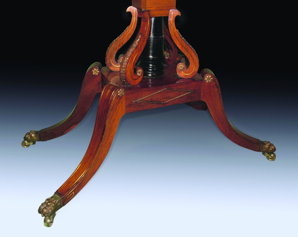 An antique Regency period card table made of dark rosewood with satinwood crossbanding, resting on an intricate scroll pedestal base with four splayed legs ending in brass lion paw castors. View III
